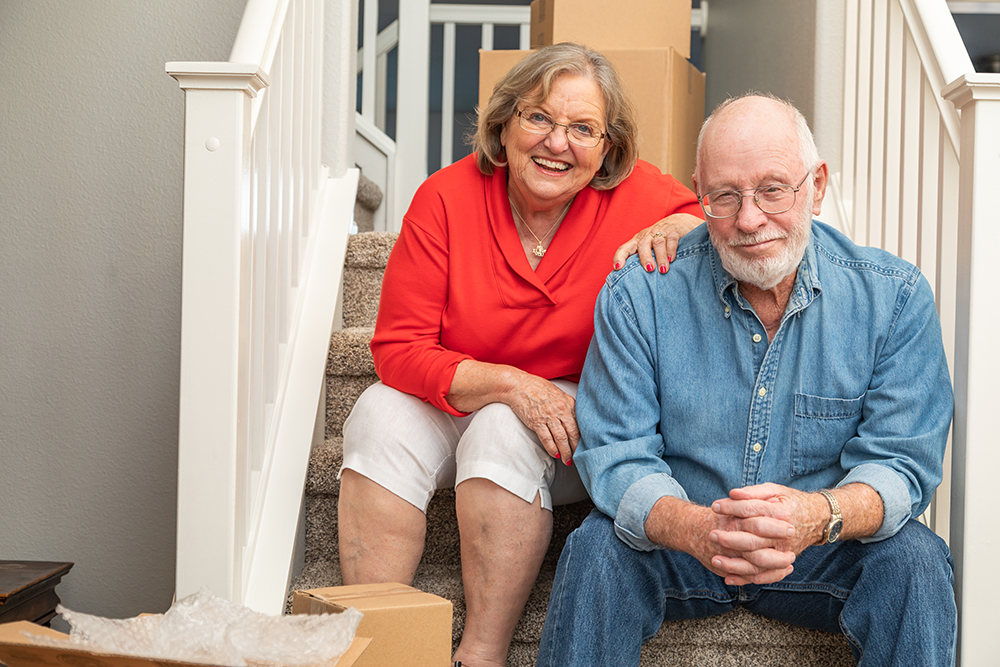 Senior Couple Resting On Stairs Surrounded By Moving Boxes.