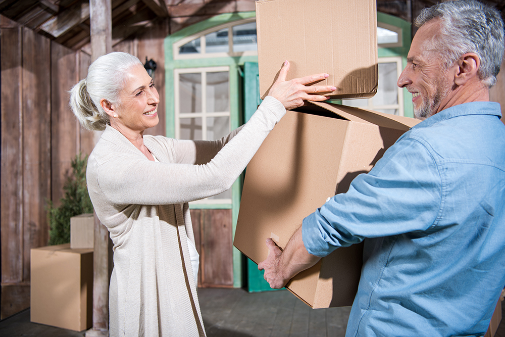 Smiling senior couple holding cardboard boxes while moving into new house