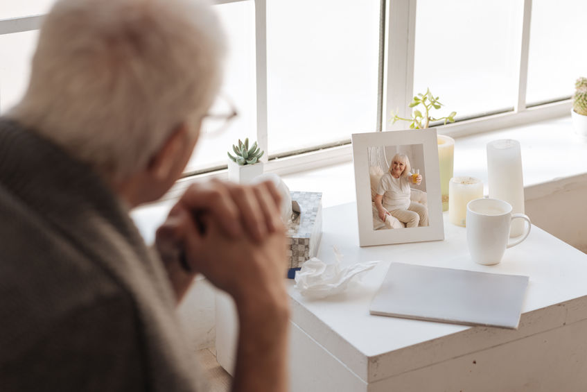 A man with dementia looking out the window with a picture of his wife on the tableside